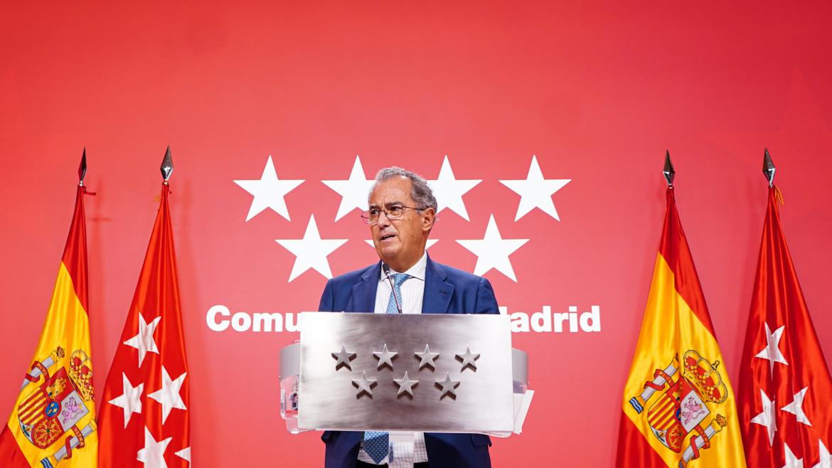 El consejero interviniendo en el atril con el logo de fondo de la Comunidad de Madrid