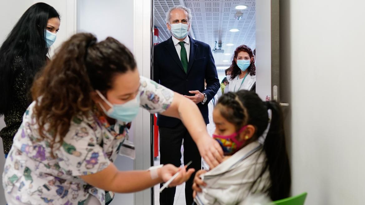 El consejero Enrique Ruiz Escudero visita el dispositivo de vacunación del Hospital de La Paz El consejero mirando como vacunan a una niña