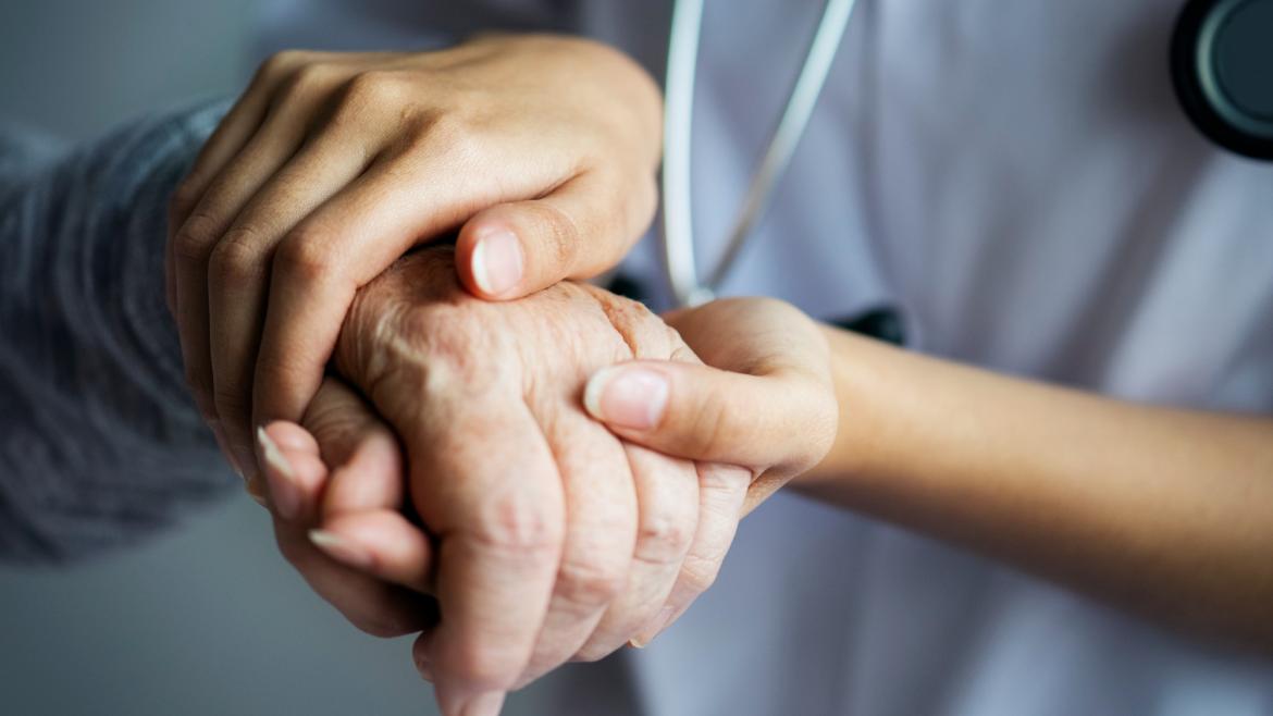 Un sanitario coge las manos de una persona mayor