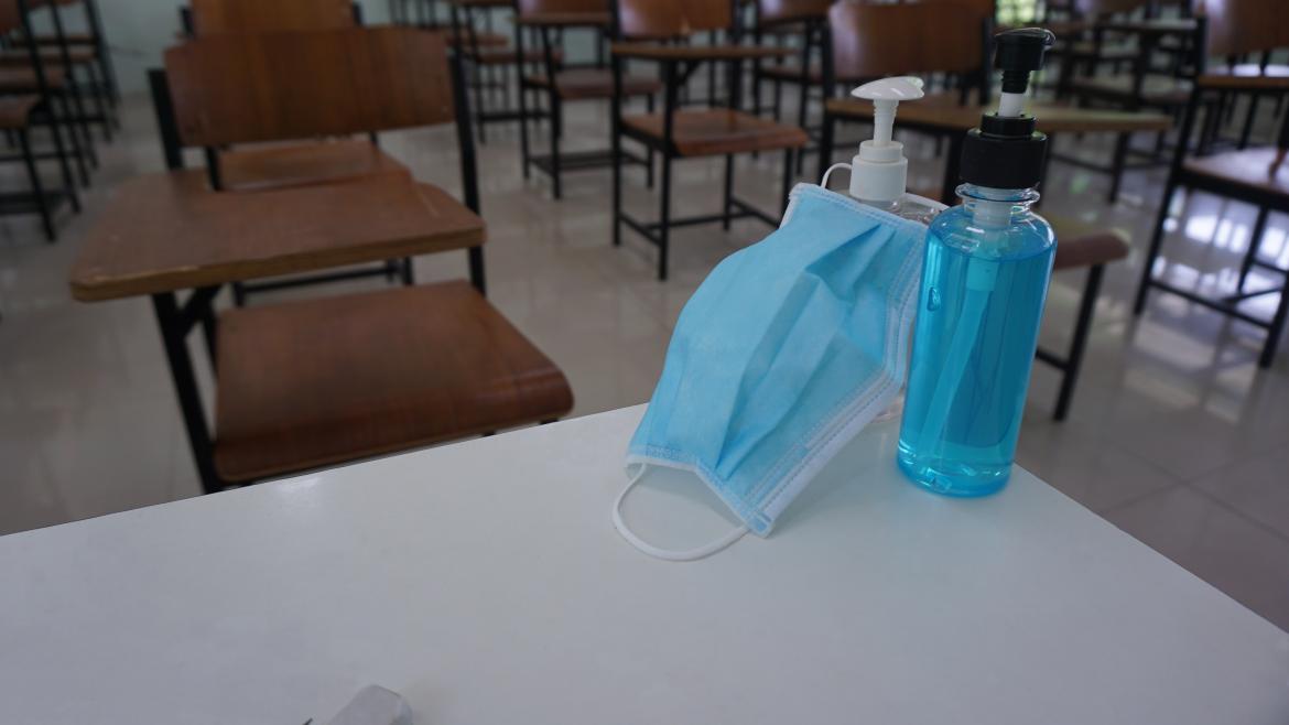 Una clase con una mascarilla y un bote de gel desinfectante