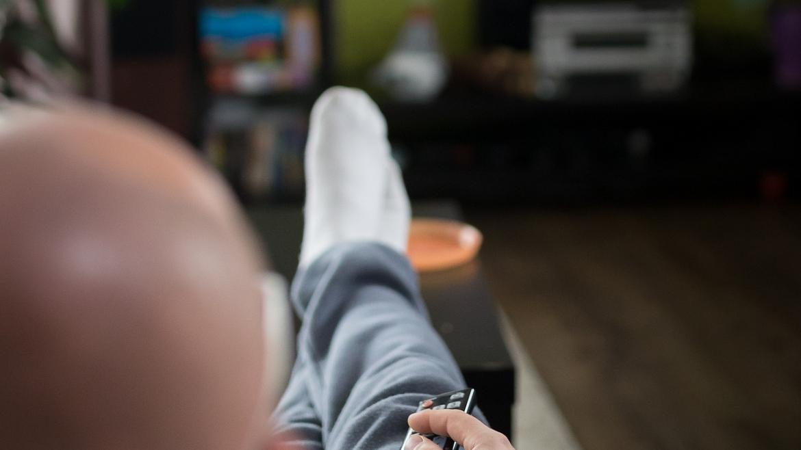 señor sentado en el sofá con el mando a distancia en la mano viendo la tv