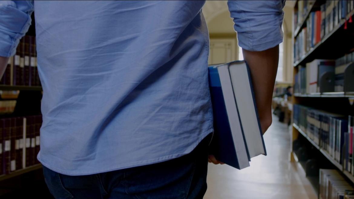 Joven de espaldas en un pasillo de biblioteca