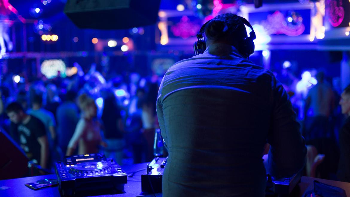 Un DJ tocando en una discoteca mientras la gente baila