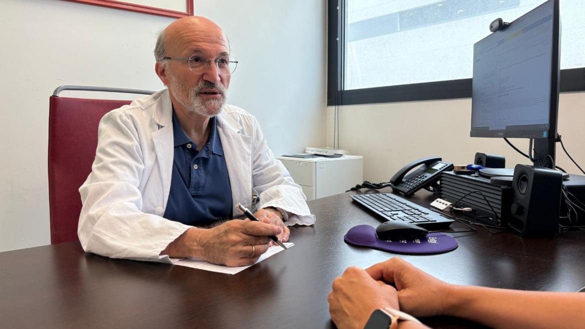 Doctor de frente atendiendo en consulta a paciente al que se le ven los brazos apoyados en mesa
