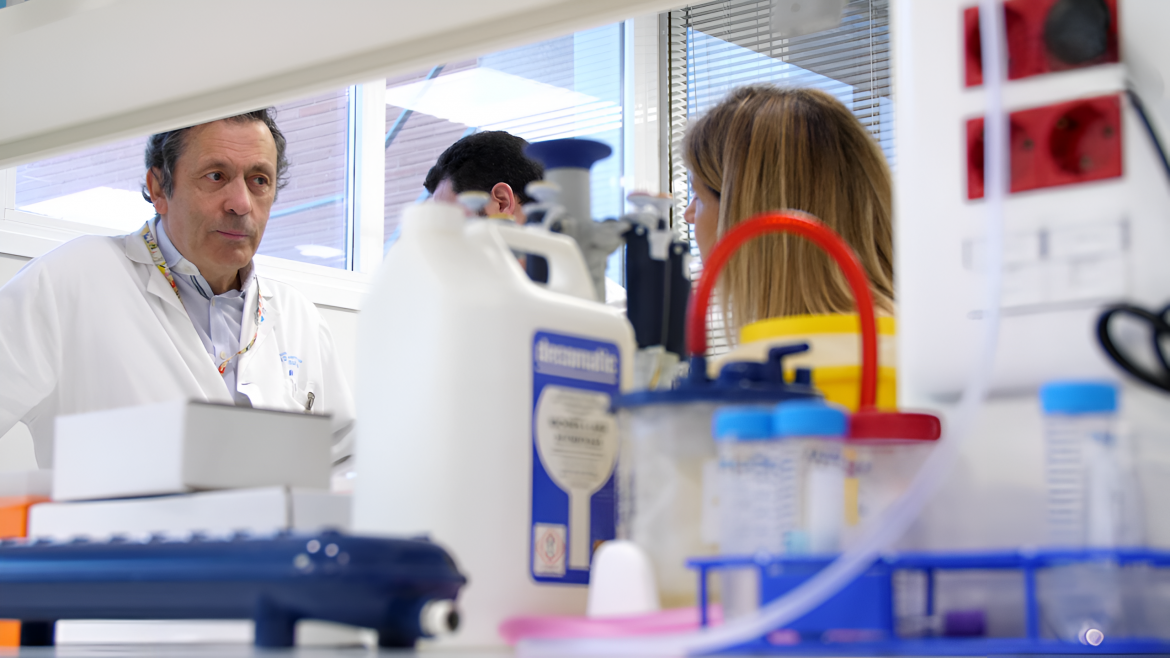 Un hombre con bata blanca en un laboratorio al fondo en primer plano material.