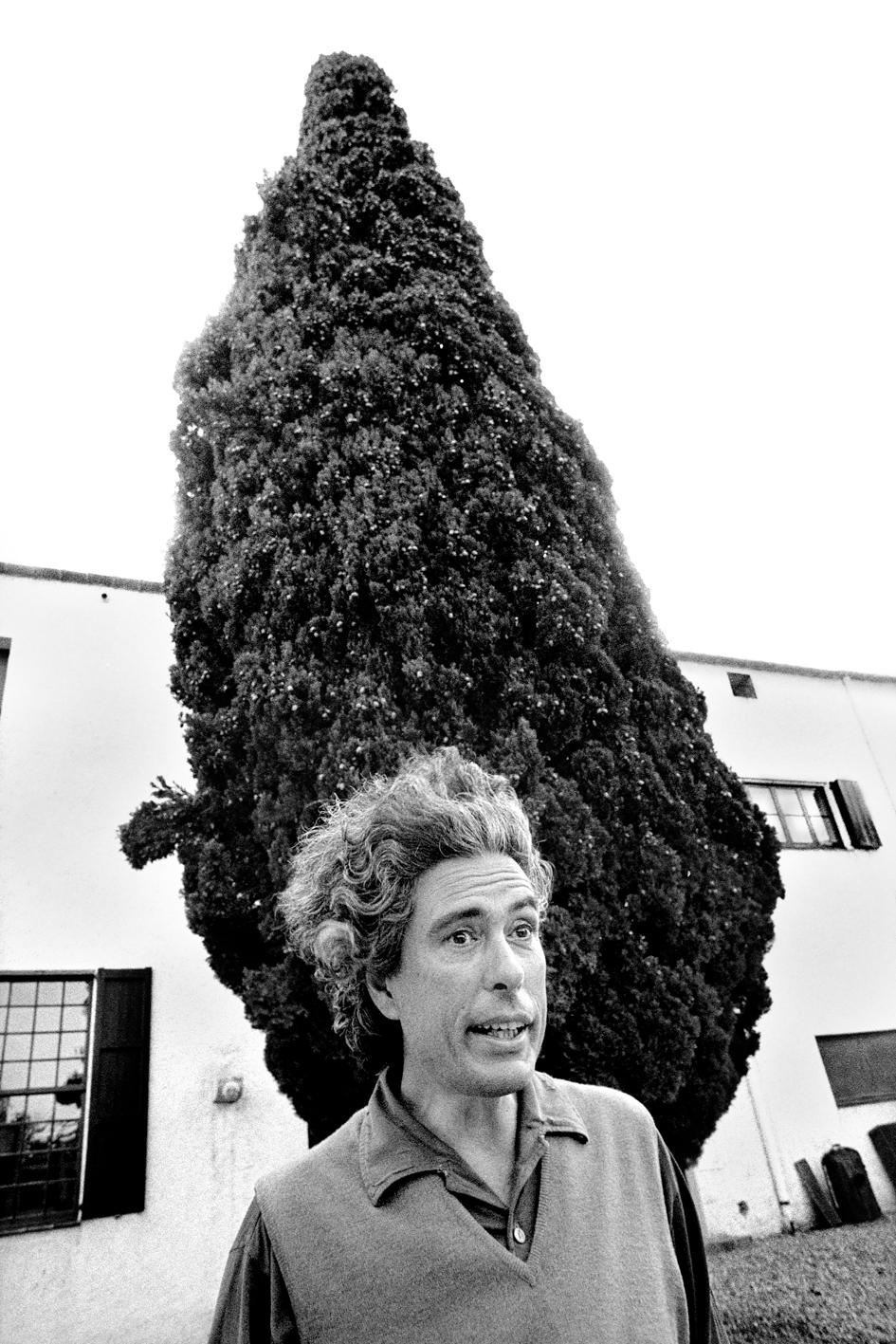 Retrato de un hombre despeinado en blanco y negro con un ciprés de fondo