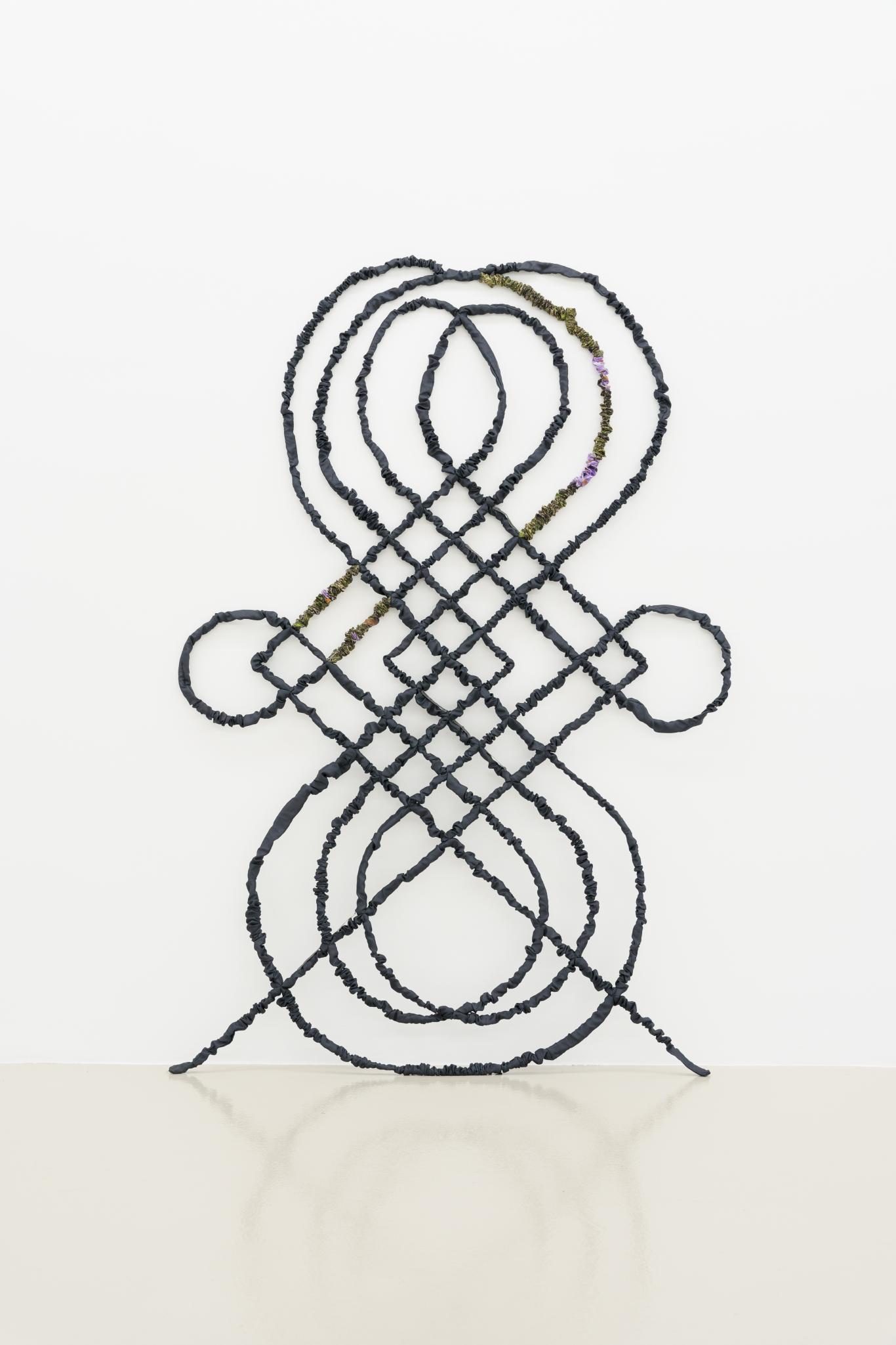 Escultura de acero y textil que tiene forma de reja con motivos curvos vegetales