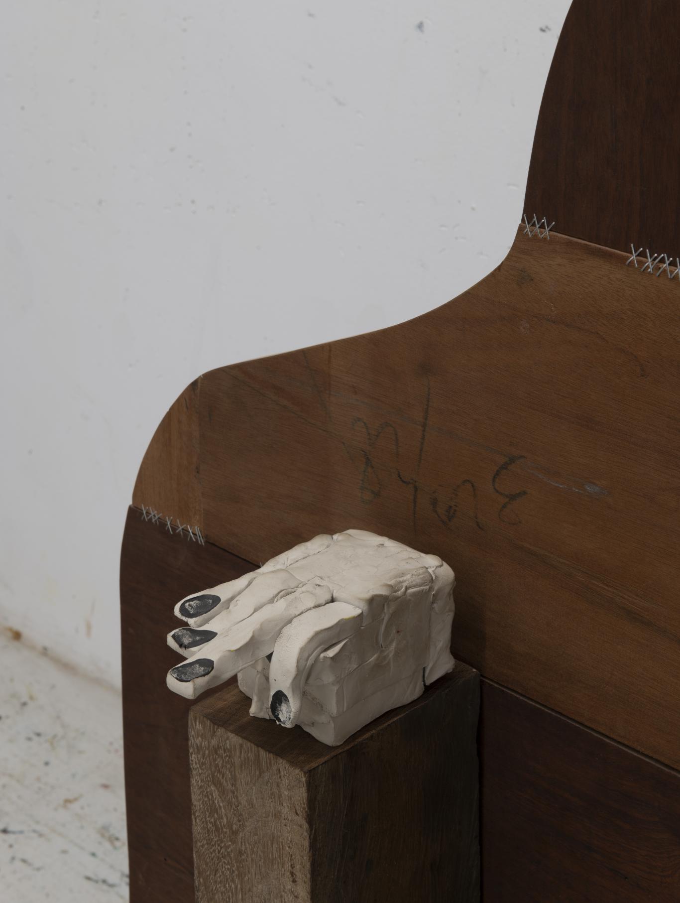 Imagen de una mano en escayola blanca sobre un banco de madera oscuro