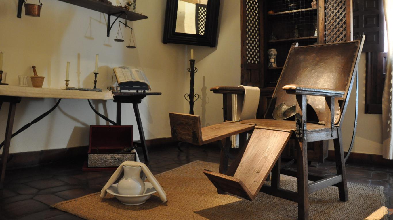 Habitación con una silla de madera y botes de farmacia antigua