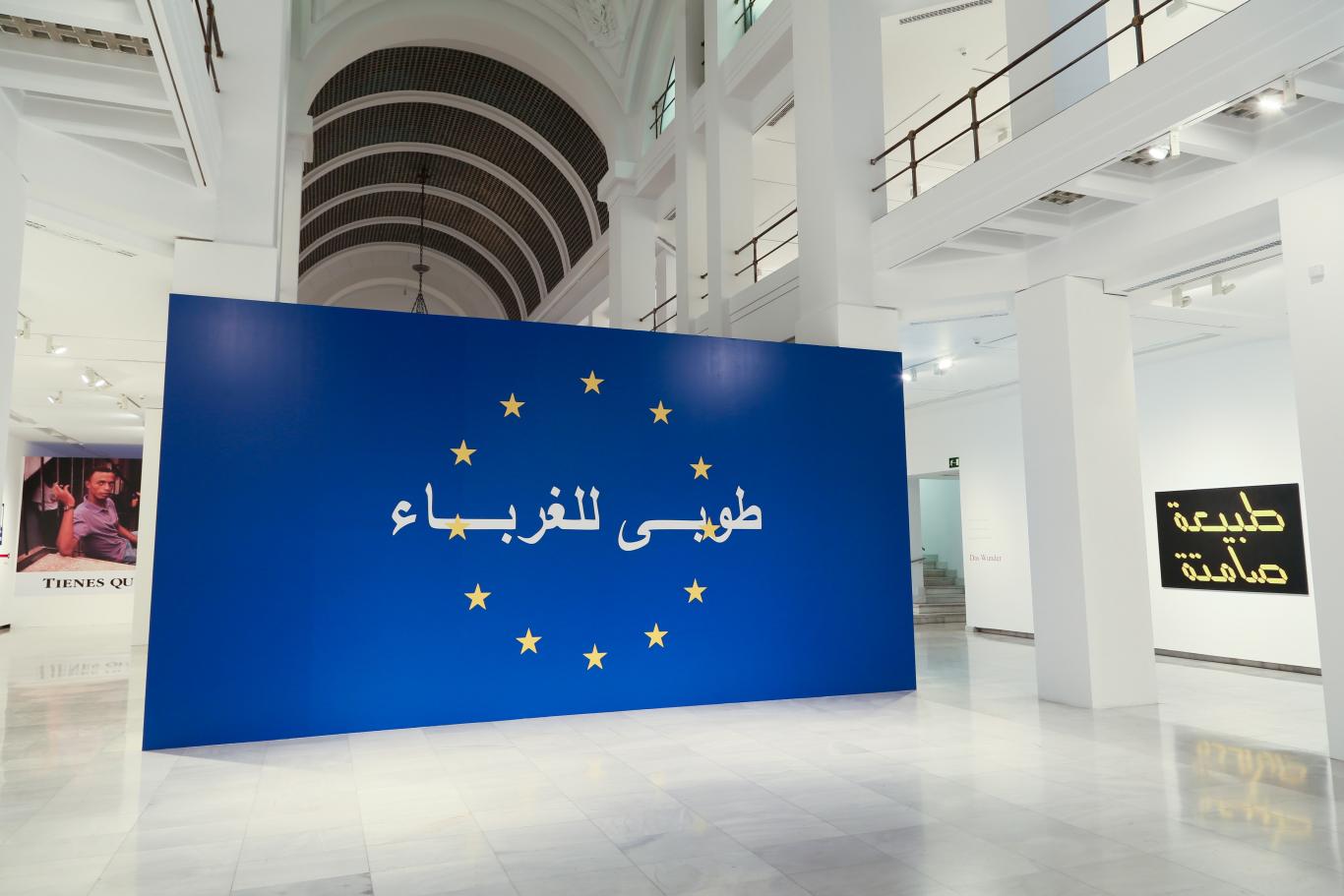 Rogelio López Cuenca. Los bárbaros Muro pintado de azul en la entrada a la Sala Alcalá 31. Se distinguen 12 estrellas en dicho panel a modo de bandera de Europa y unas letras en árabe