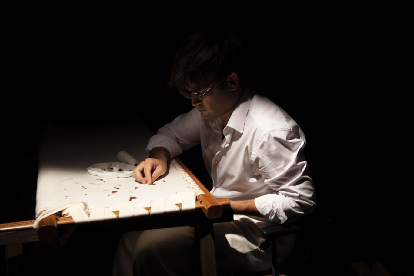 Hombre sentado haciendo encaje de bolillos bajo la luz de un flexo