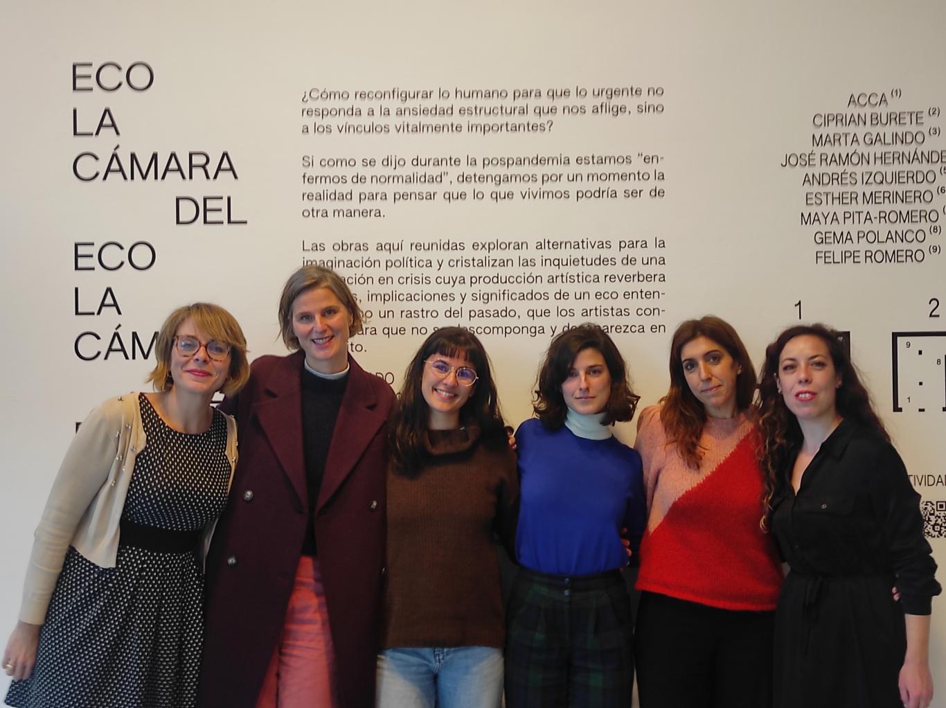 Grupo de mujeres posando frente a un vinilo en la pared donde aparece el título de la exposición