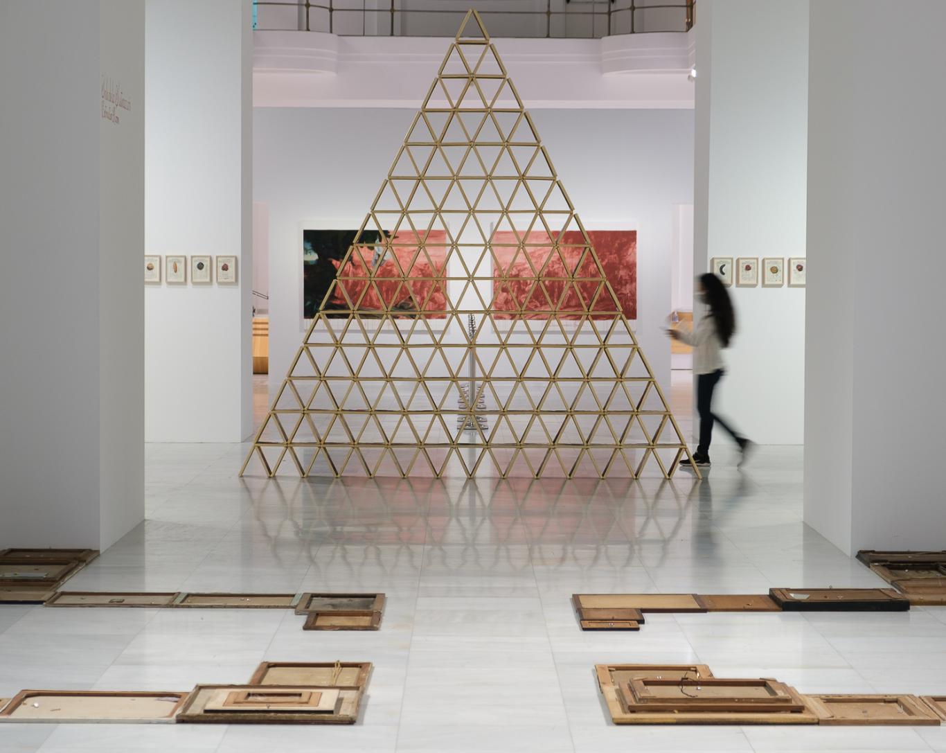 Exposición "Buen Gobierno. Sandra Gamarra Heshiki" Foto: Guillermo Gumiel Mujer atravesando una exposición donde hay una pirámide hecha con naipes