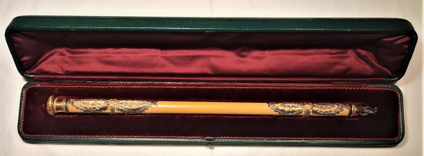 batuta cilíndrica con adornos en plata sobre estuche de terciopelo rojo