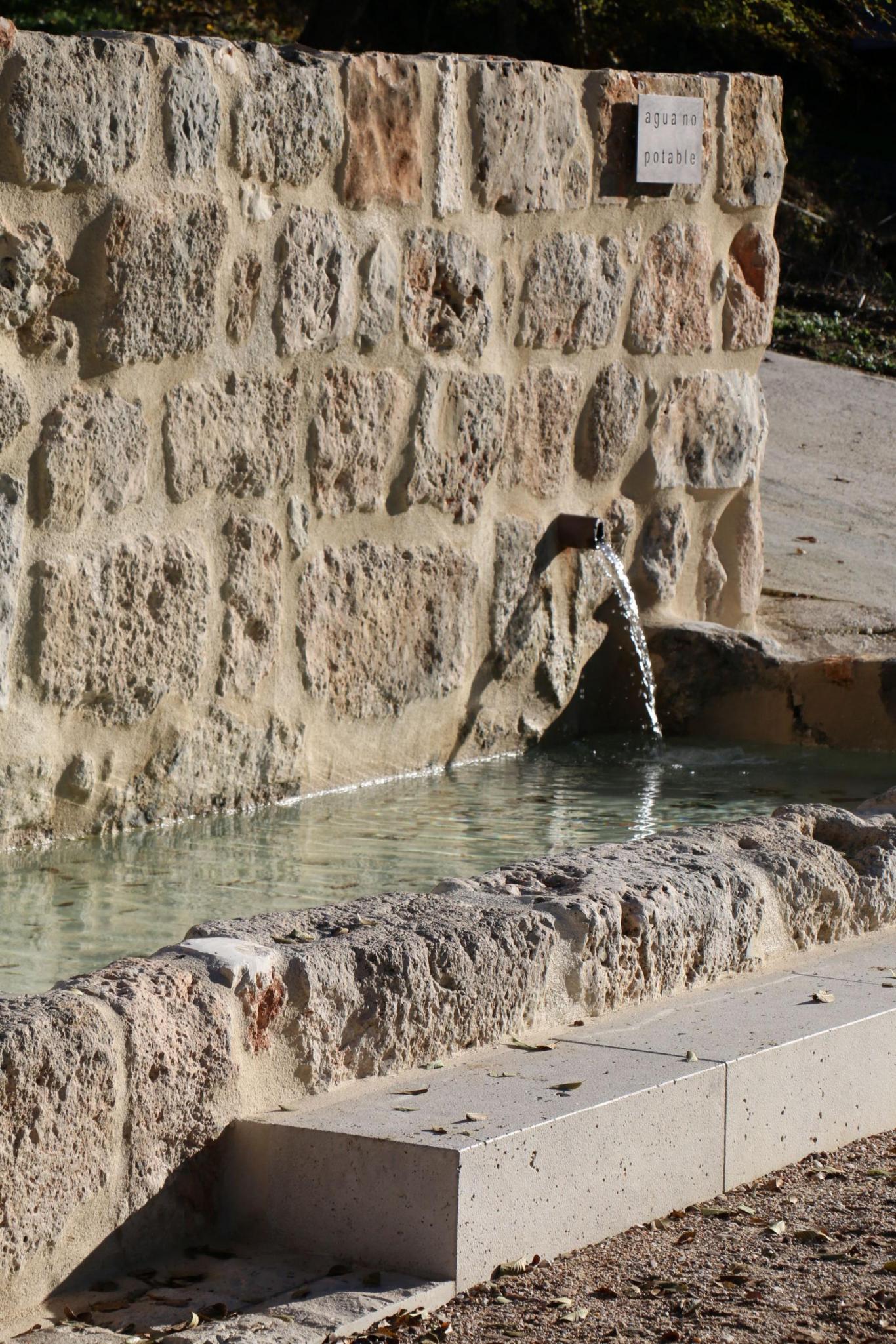 imagen de una fuente de piedra con caño metálico por el que sale el agua hacia un pilón