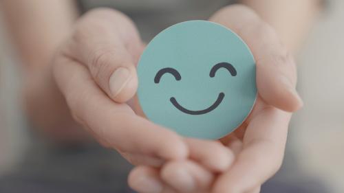 Primer plano de unas manos sujetando un emoticono verde sonriente