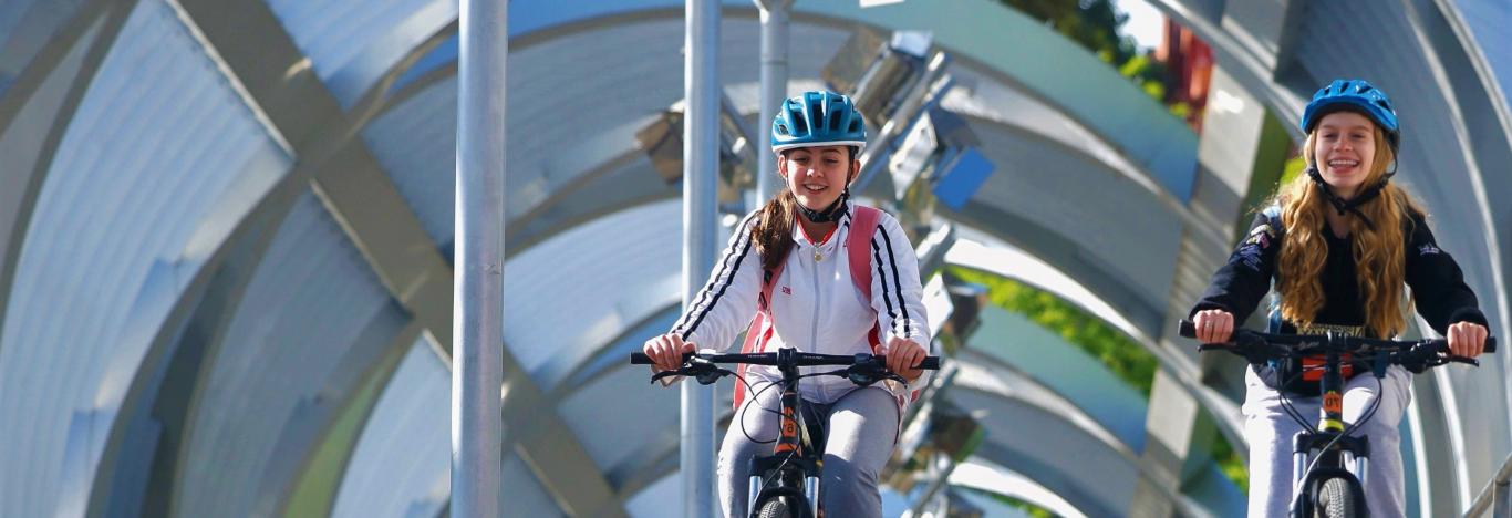 Niñas en bibicleta por un puente con estructura metálica