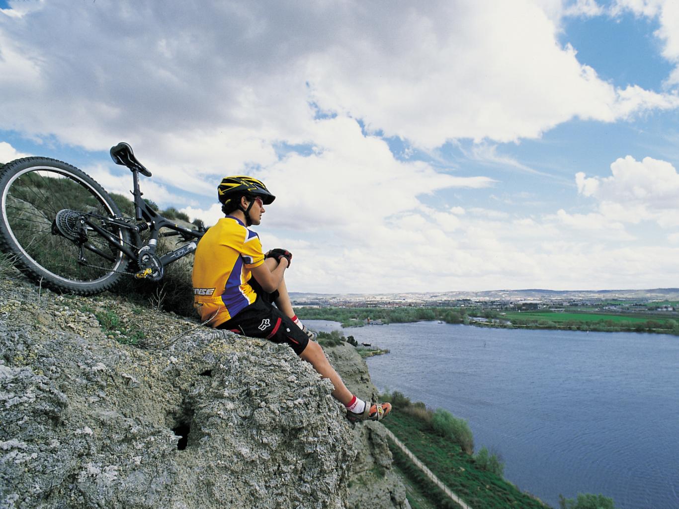 Ciclista sentado entre las rocas sobre la laguna de El Campillo