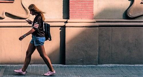 Chica andando por una acera con un móvil