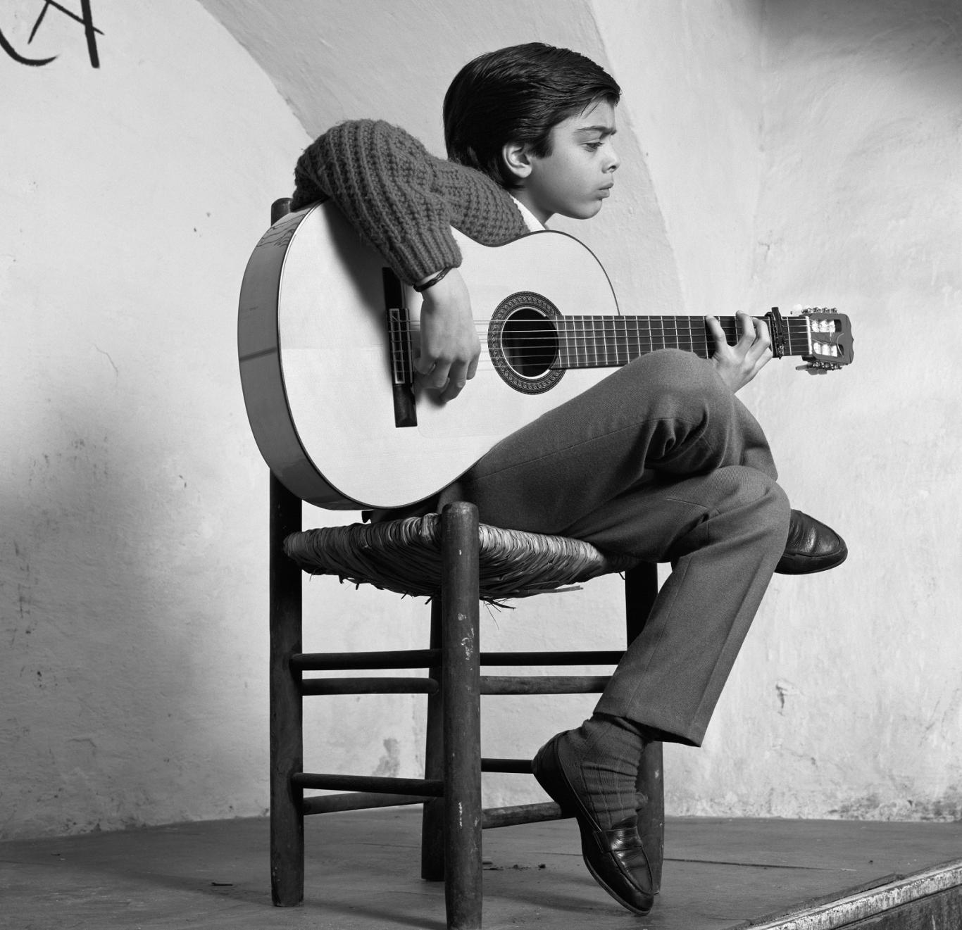 Niño sentado en una silla tocando una guitarra clásica