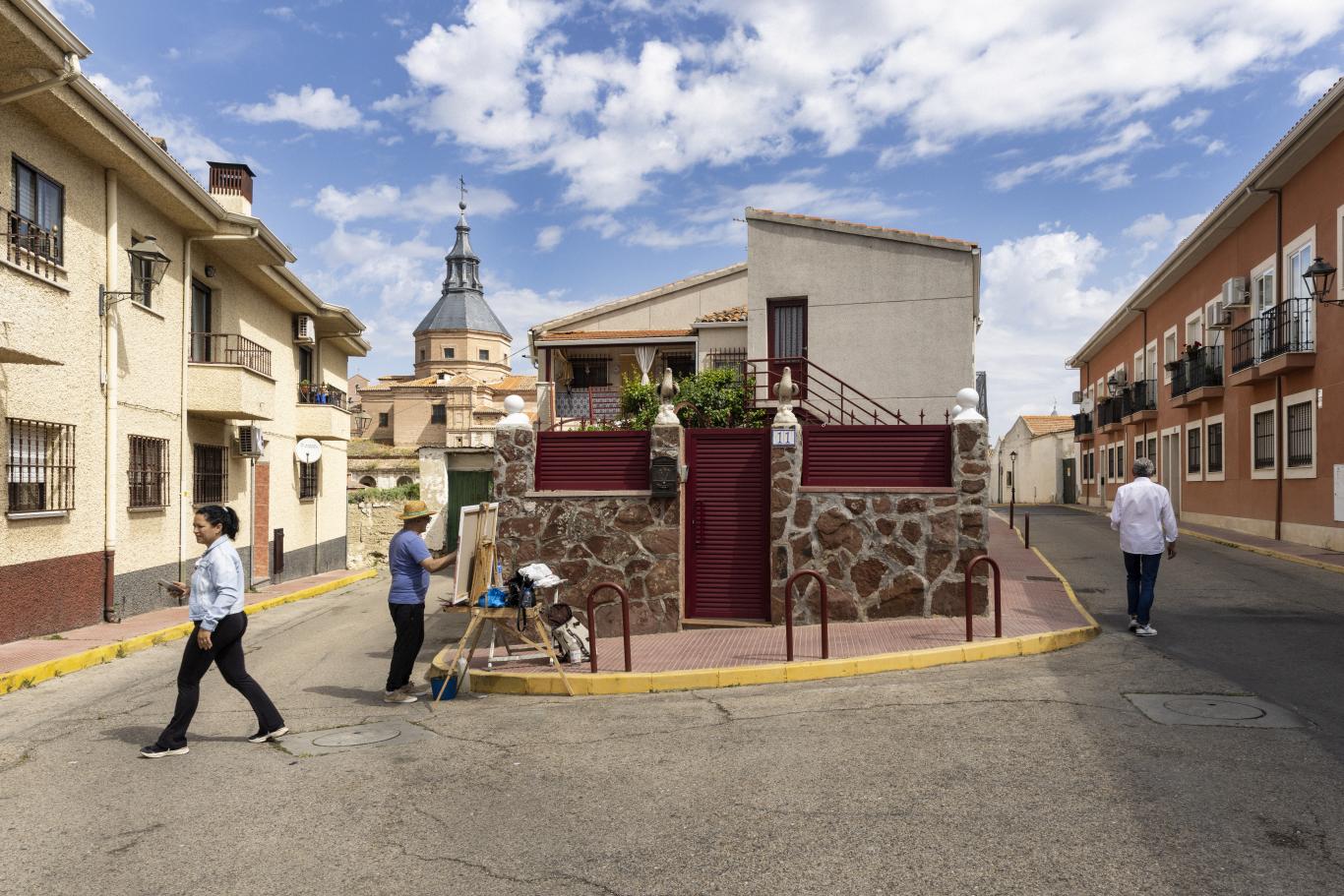 Calles de Loeches, al fondo la iglesia, en primer plano una persona pintando un cuadro apoyado en un caballete sobre la acera