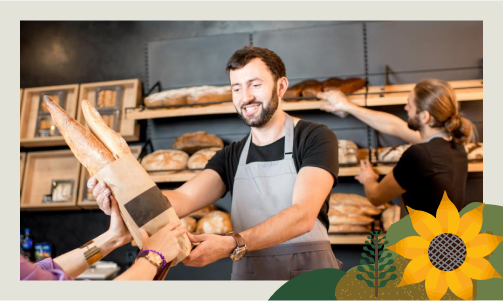 Fotografía de un dependiente de una panadería entregando a un cliente una barra de pan