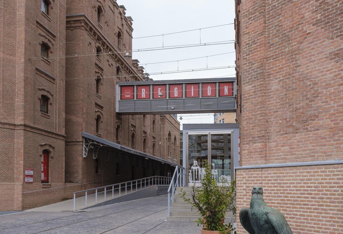 Dos de los edificios del complejo cultural El Águila, en la ventanas de la pasarela se muestra el nombre de la exposición