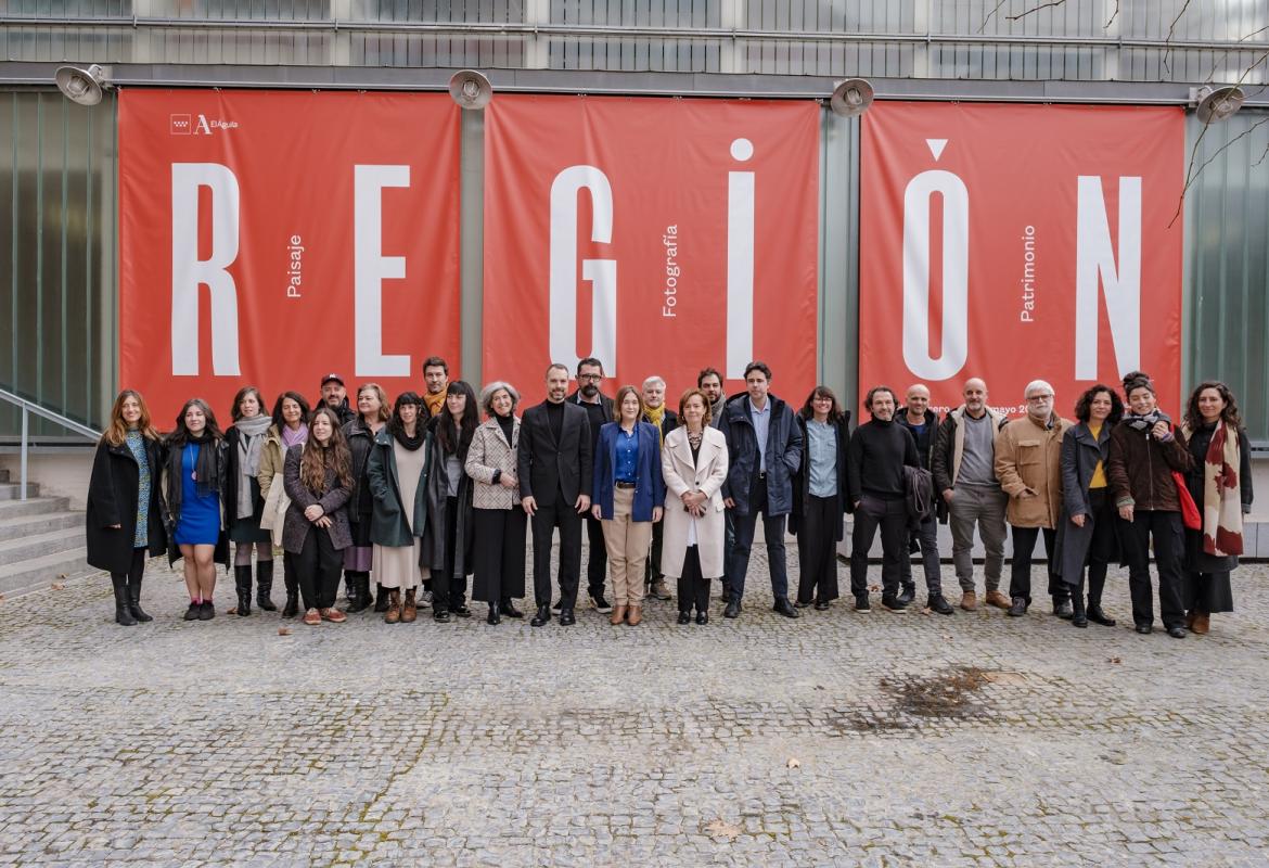 Fotografía de grupo en el exterior de la sala de exposiciones, tras el grupo el cartel de la exposición REGIÓN, Paisaje, fotografía y patrimonio
