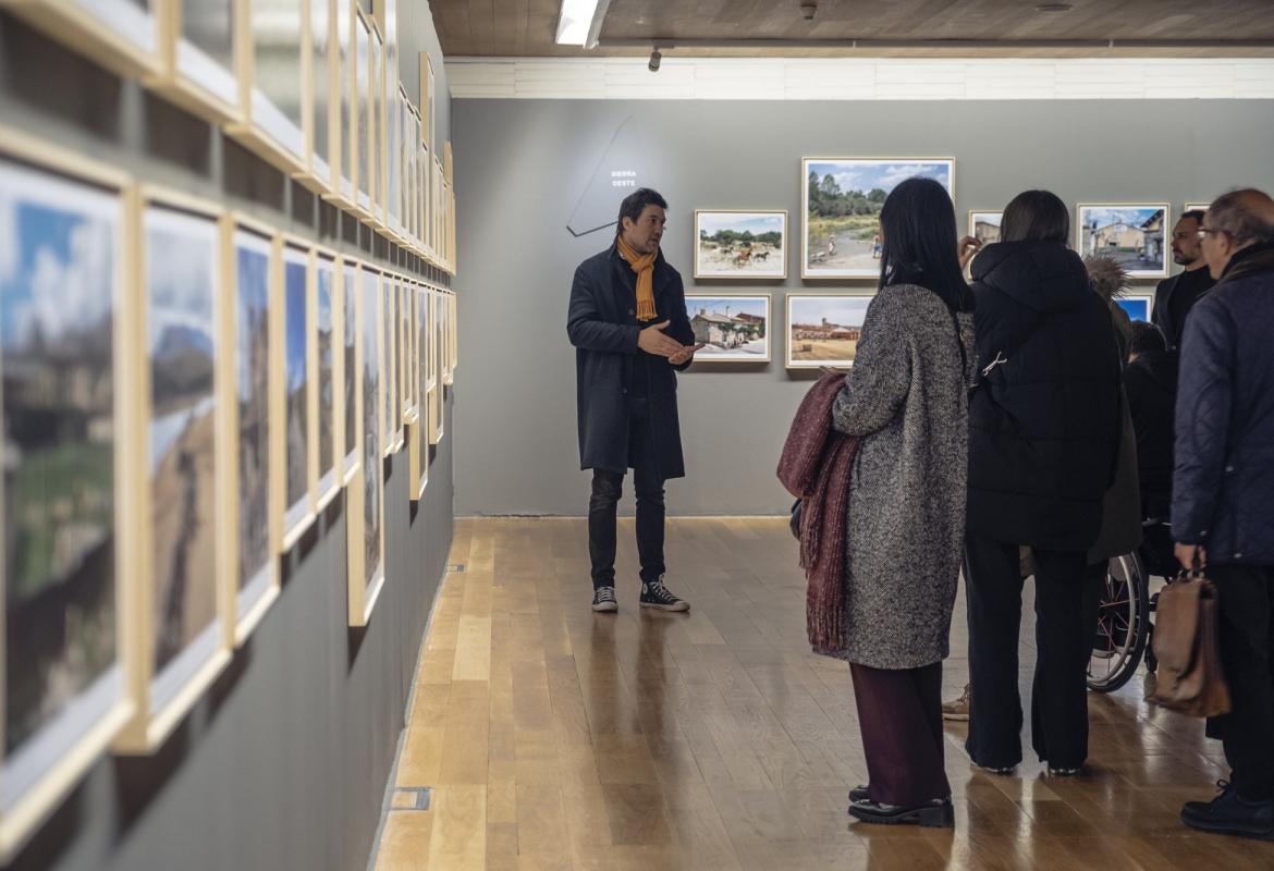 Una persona explica la exposición REGIÓN, Paisaje, fotografía y patrimonio a un grupo de visitantes 