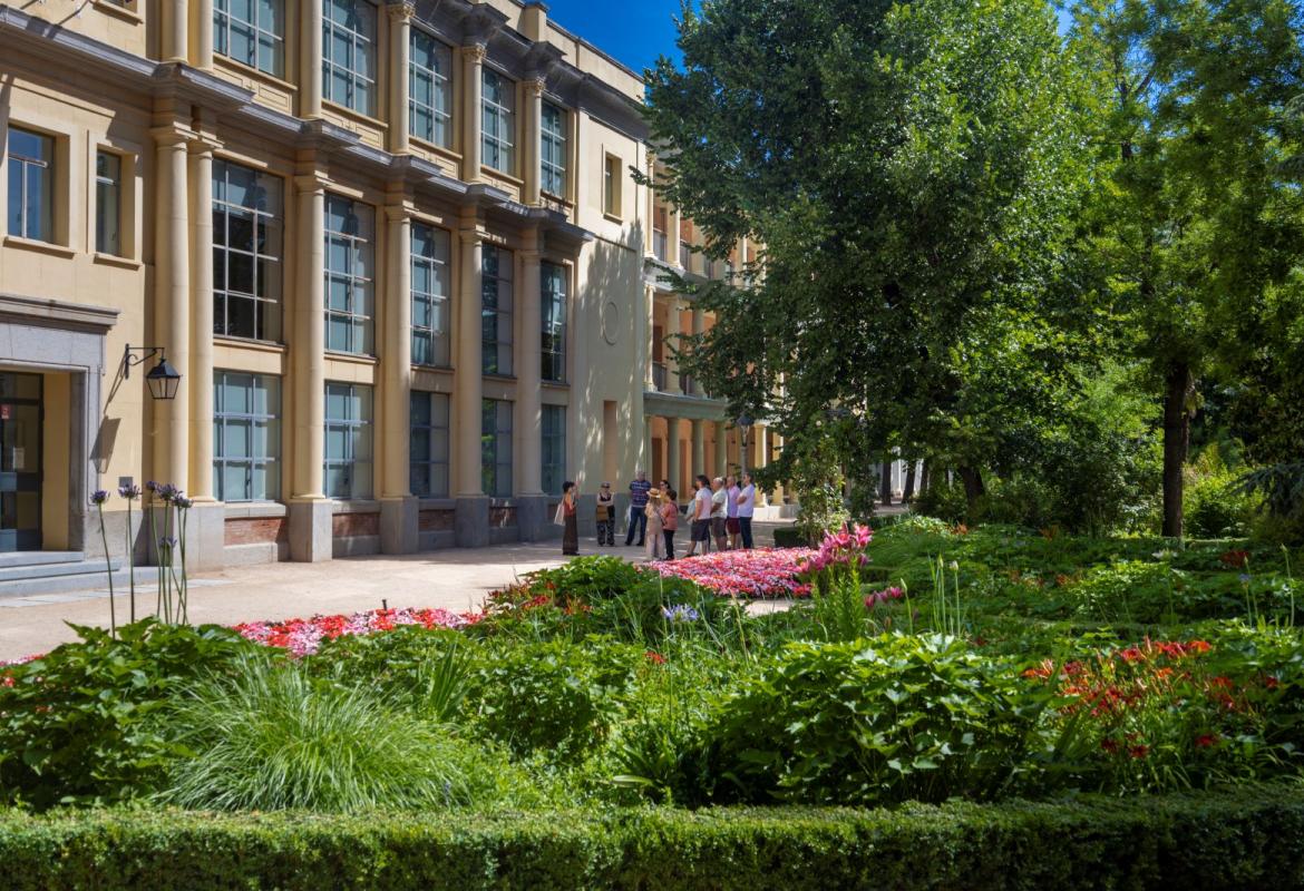 grupo de personas de espaldas en una visita guiada en un jardín junto a un edificio de columnas