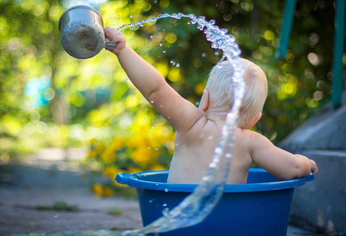 Niño dentro de un barreño echando agua con un cazo