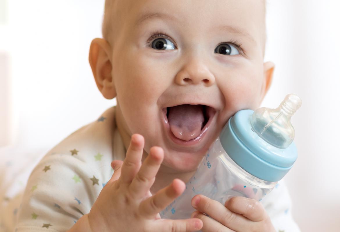 Bebé sonriendo con un biberón en la mano