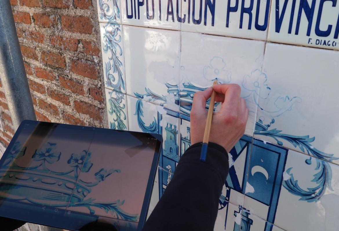 Azulejos sobre fachada de ladrillo en mal estado, una mano en primer plano sosteniendo un pincel