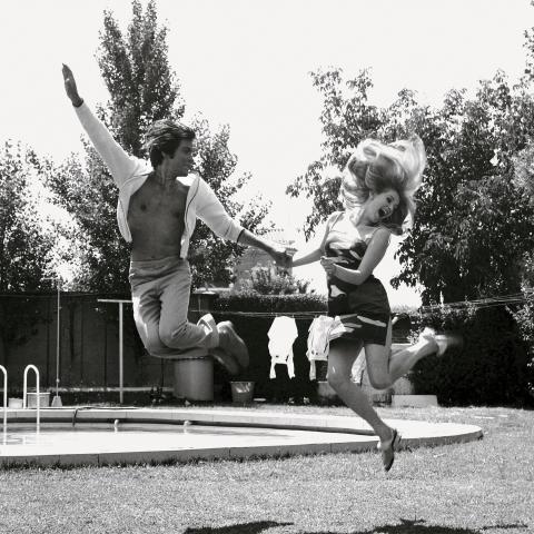 imagen de una pareja en un jardín saltando en el aire mientras se da de la mano