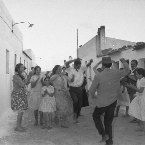 Un grupo de hombres, mujeres y niños bailando flamenco y dando palmas en un poblado