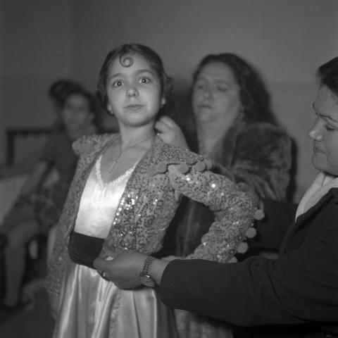 Niña a la que dos mujeres están colocando una torerilla y un colgante con una cruz