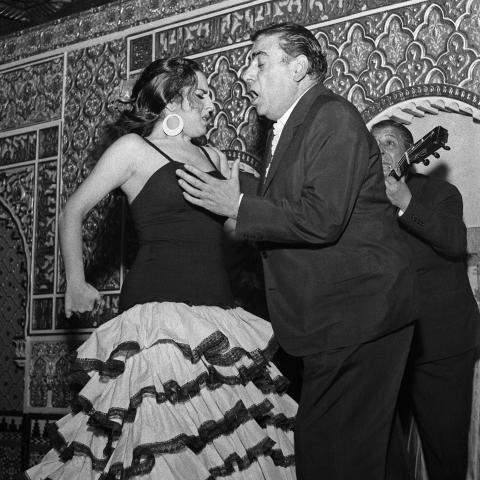 Hombre y mujer con traje de flamenca bailan y cantan acompañados por un hombre tocando la guitarra clásica