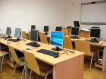 Aula de formación con mesas y ordenadores y pantalla pizarra al frente
